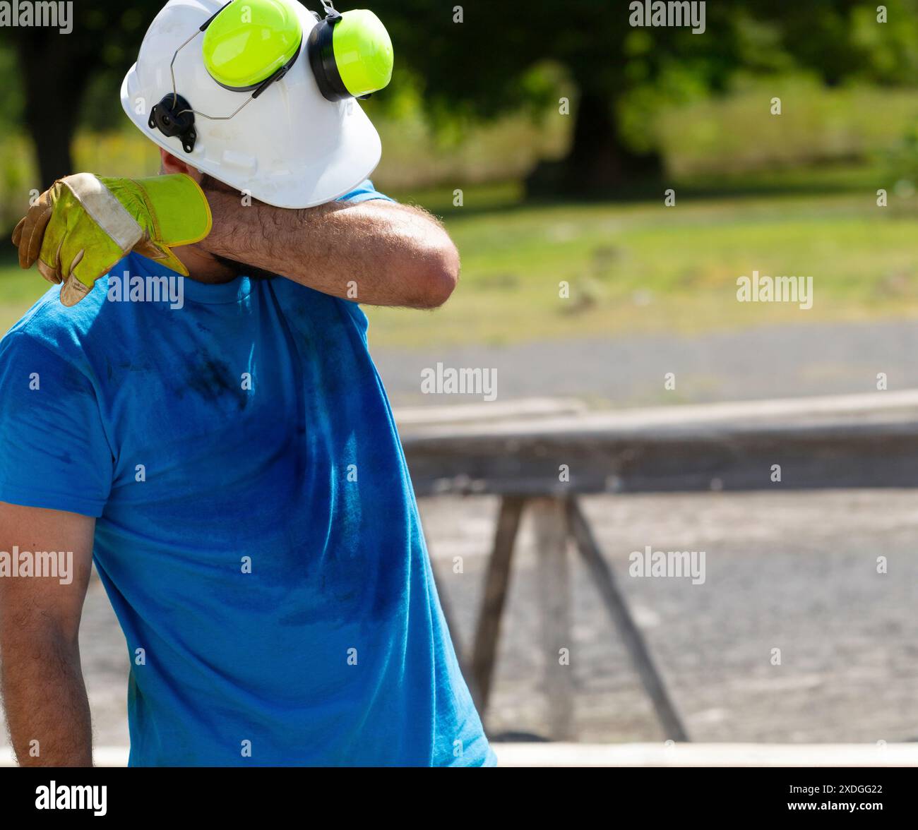 Ein nicht identifizierbarer Mann in blauem Hemd und weißem Hardhat wischt den Schweiß von seinen Brauen ab, während er an heißen Tagen beim Bau arbeitet. Stockfoto