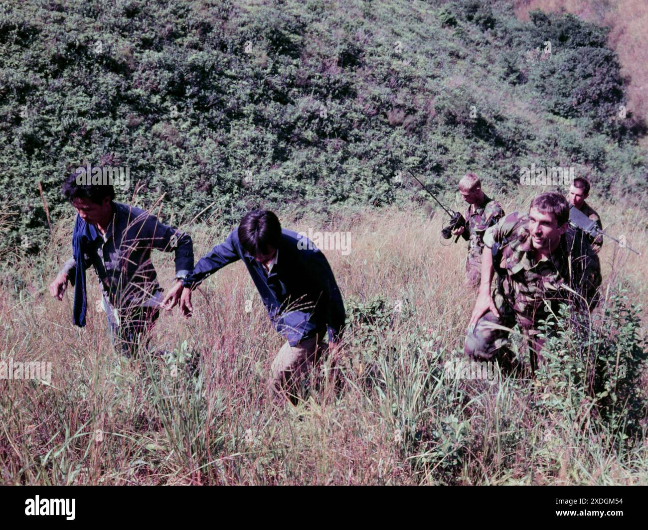 Zwei männliche illegale Einwanderer („IIS“), die gerade in Hongkong verhaftet wurden, werden von zwei Soldaten des Cheshire Regiment, der britischen Armee, auf den Robin's Nest, einen Hügel in der Nähe der Grenze in den New Territories von Hongkong, begleitet. Okt. 1984. Der Soldat links trägt ein altmodisches Radio-Paket. Stockfoto