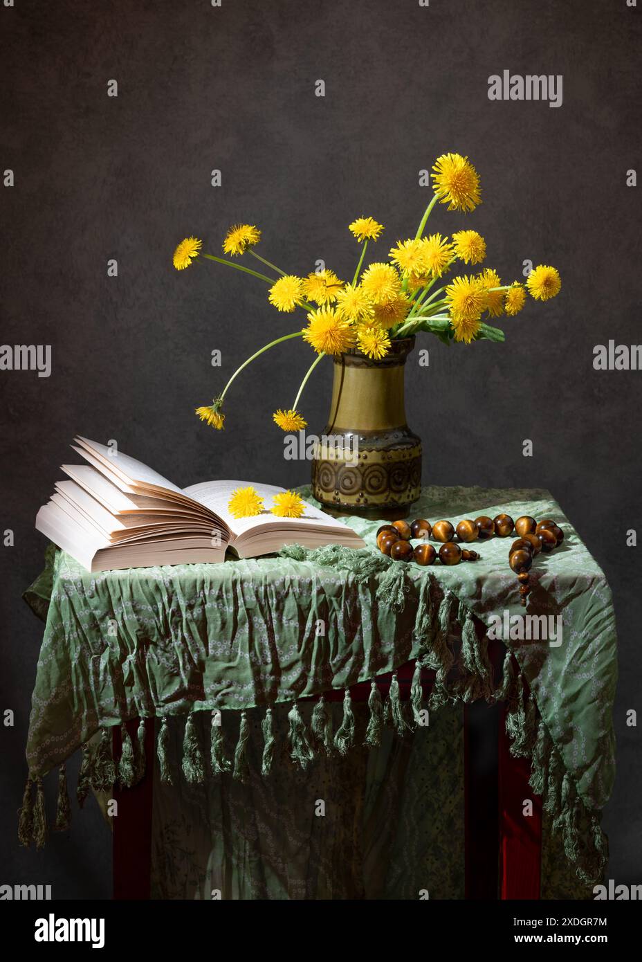 Gelber Löwenzahn in einer Vase und ein offenes Buch auf dem Tisch Stockfoto