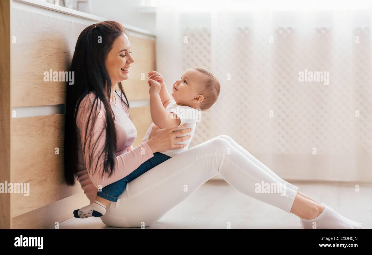 Frau Mutter, die das Baby hält, während sie auf dem Boden sitzt Stockfoto