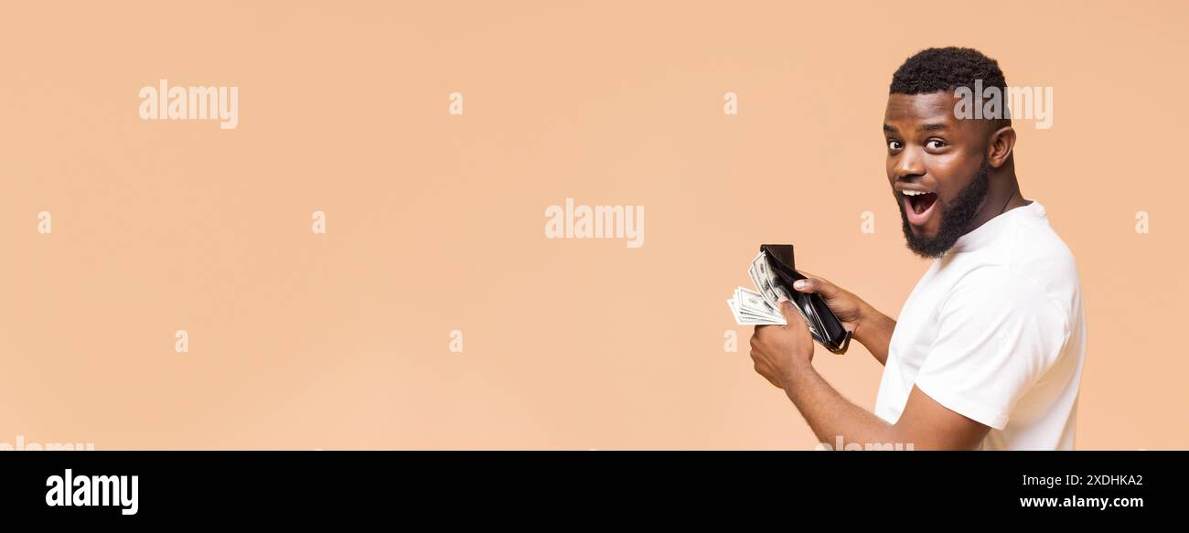 Aufgeregter Mann, der Bargeld und Geldbörse vor Peach-Hintergrund hält Stockfoto