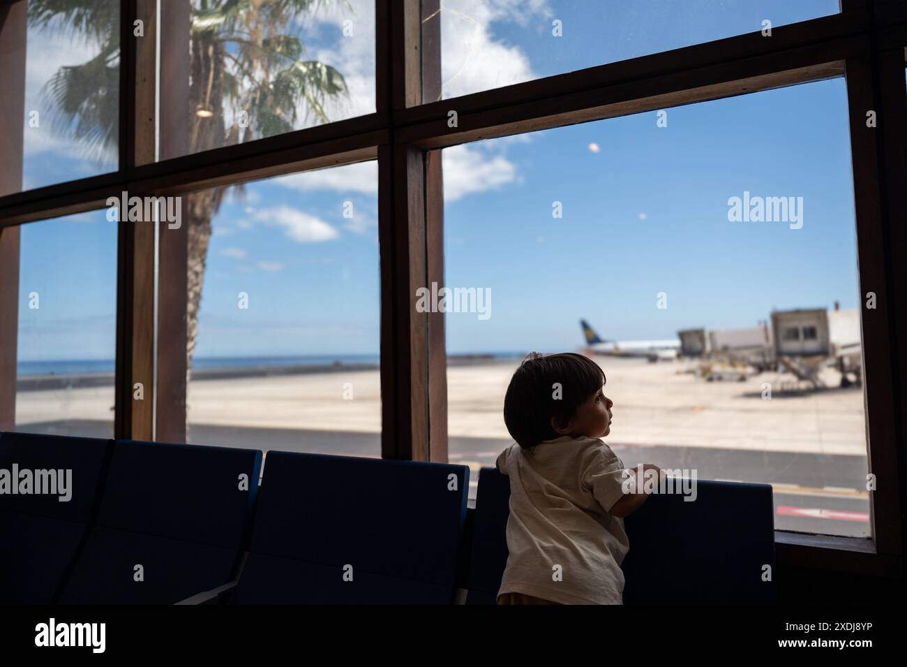 Kind beobachtet die Flugzeuge durch die Fenster des Flughafens und klettert auf die Sitze Stockfoto