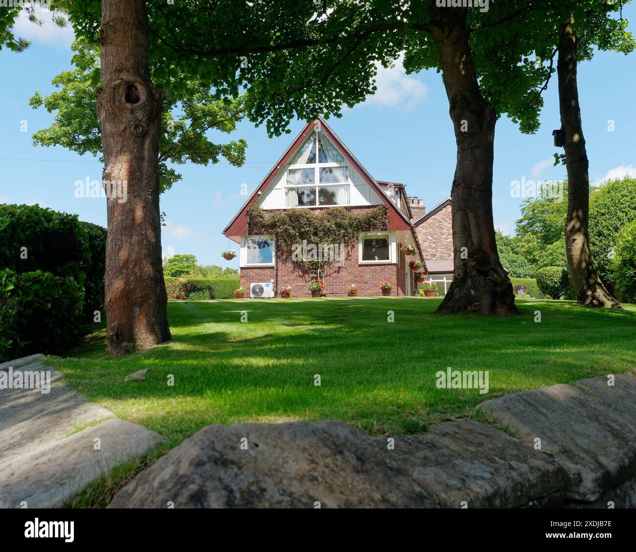Modernes Haus mit markantem Spitzdach und großem Garten mit Bäumen in Biddulph, Staffordshire, England. Juni 2024 Stockfoto
