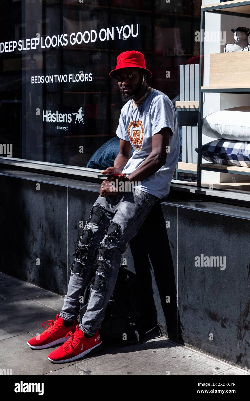 Schwarzer junger Mann mit roter Mütze, passend zu roten Turnschuhen, London, England, Großbritannien. Stockfoto