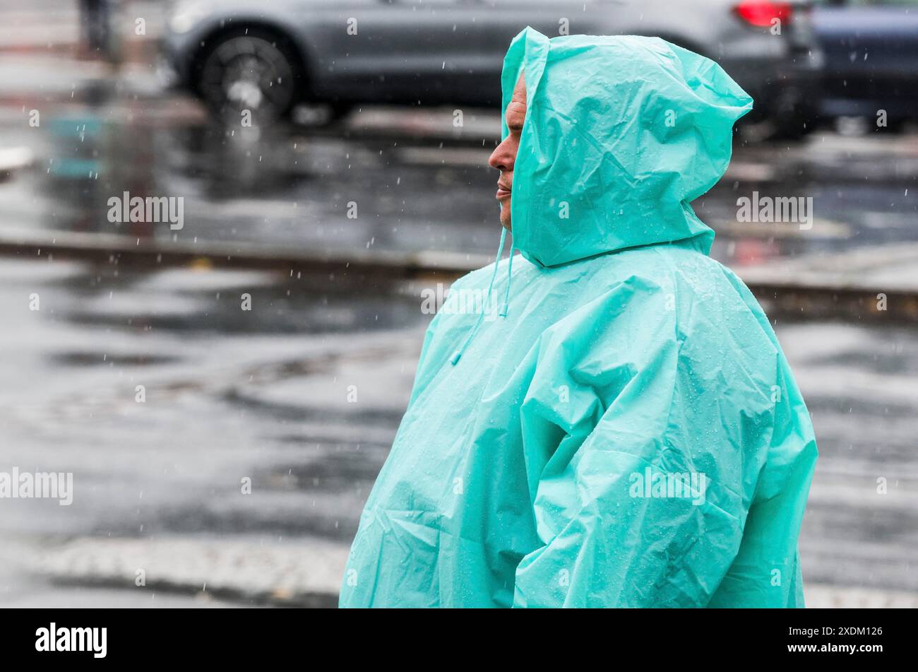 Ein Mann mit einem regenumhang steht auf einer Straße bei starkem Regen, Berlin, 22.06.2024, Berlin, Berlin, Berlin, Deutschland Stockfoto