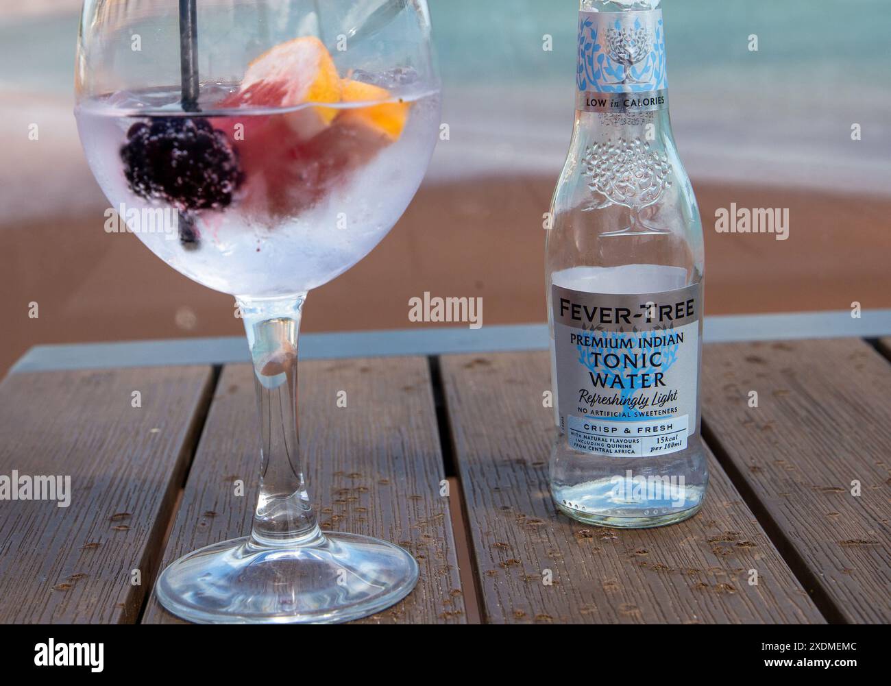 Nahaufnahme eines Gin Tonic Cocktails mit Früchten und einer Flasche Fever-Tree Tonic Water auf einem Holztisch Stockfoto