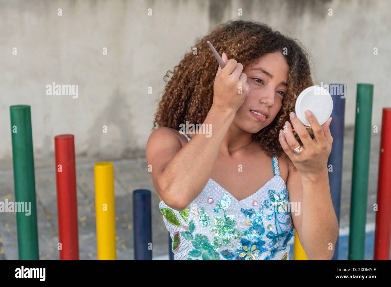 Junge Frau mit lockigem Haar, die sich mit einem Handspiegel schminkt Stockfoto
