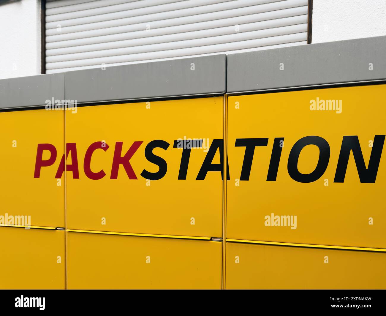 Kehl, Deutschland - April 2024: Nahaufnahme eines gelben Schildes mit dem Wort Packstation in schwarz-roten Buchstaben. Das Schild ist an einem Gebäude mit einem grauen Dach und einer weißen Wand im Hintergrund angebracht. Stockfoto