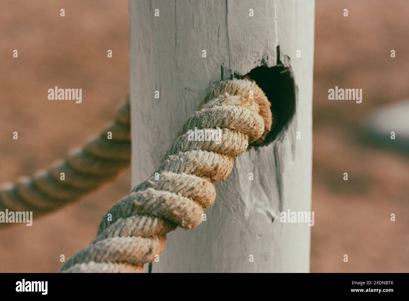 Weißes Seil aus Bio-Baumwolle auf einem weißen Holzzaun, Tor an einem Sandstrand. Hintergrund für Pfosten und Seile. Nautisches Sommerthema. Stockfoto