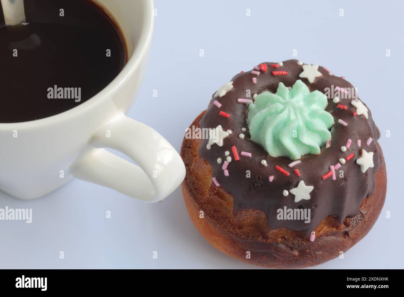 Mit Schokolade überzogener Kuchen mit dekorativem Belag. In der Nähe gibt es eine Tasse Kaffee. Stockfoto