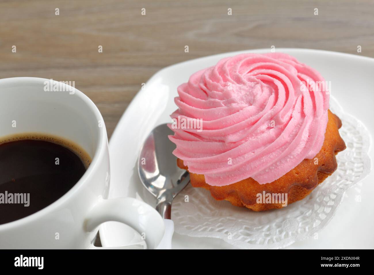 Creme Kuchen und eine Tasse Kaffee. Der Kuchen liegt auf einer Untertasse. In der Nähe eines Kaffeelöffels. Stockfoto