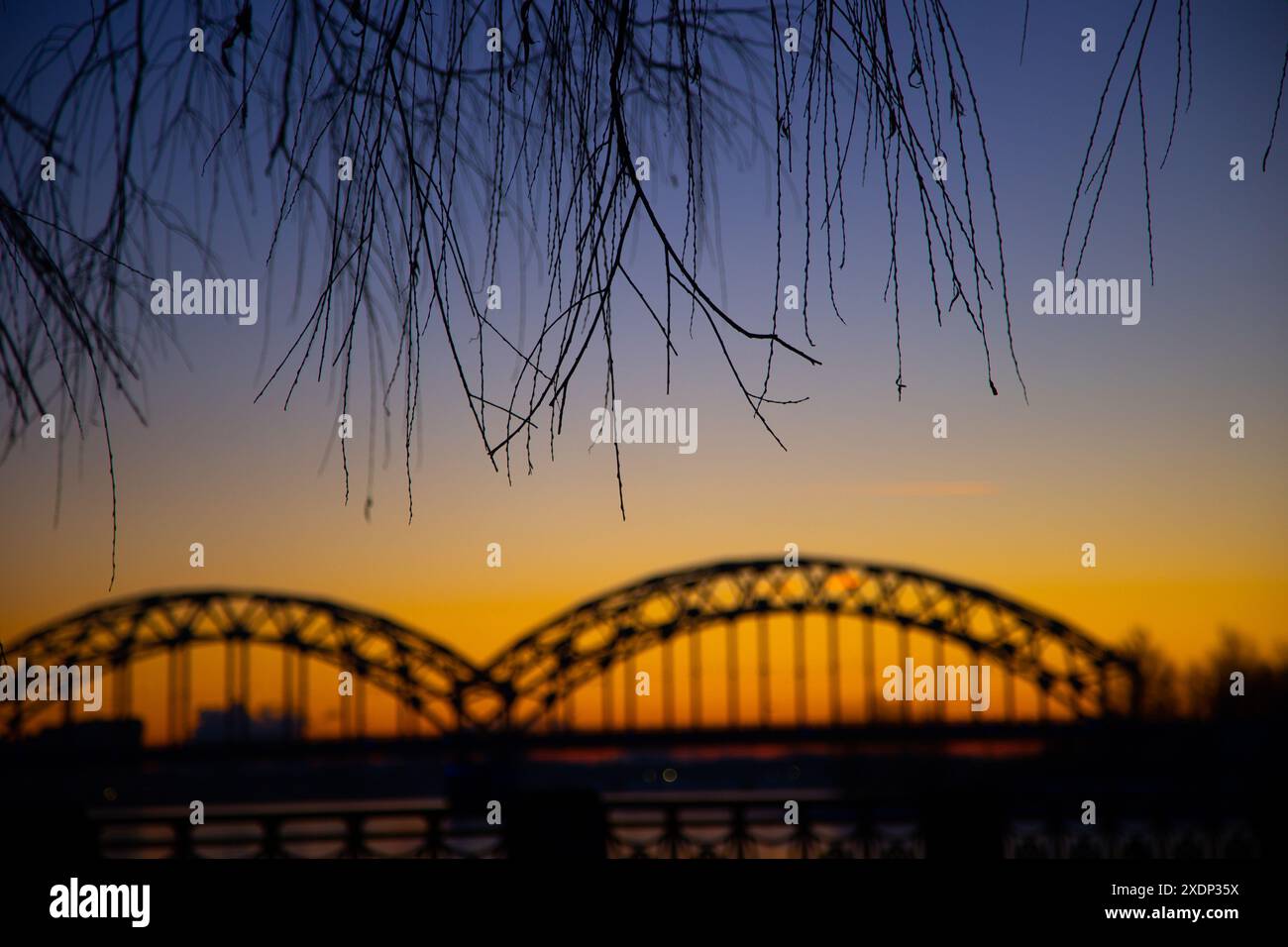 Eine wunderschöne Landschaft bei Sonnenaufgang mit eiserner Brücke über den gefrorenen Fluss Daugava in der lettischen Hauptstadt Riga. Winterlandschaft Nordeuropas. Stockfoto