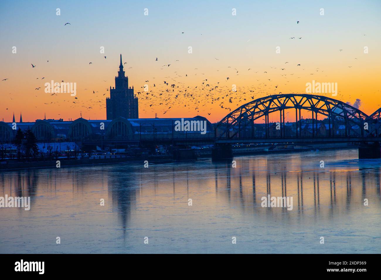 Eine wunderschöne Landschaft bei Sonnenaufgang mit eiserner Brücke über den gefrorenen Fluss Daugava in der lettischen Hauptstadt Riga. Winterlandschaft Nordeuropas. Stockfoto