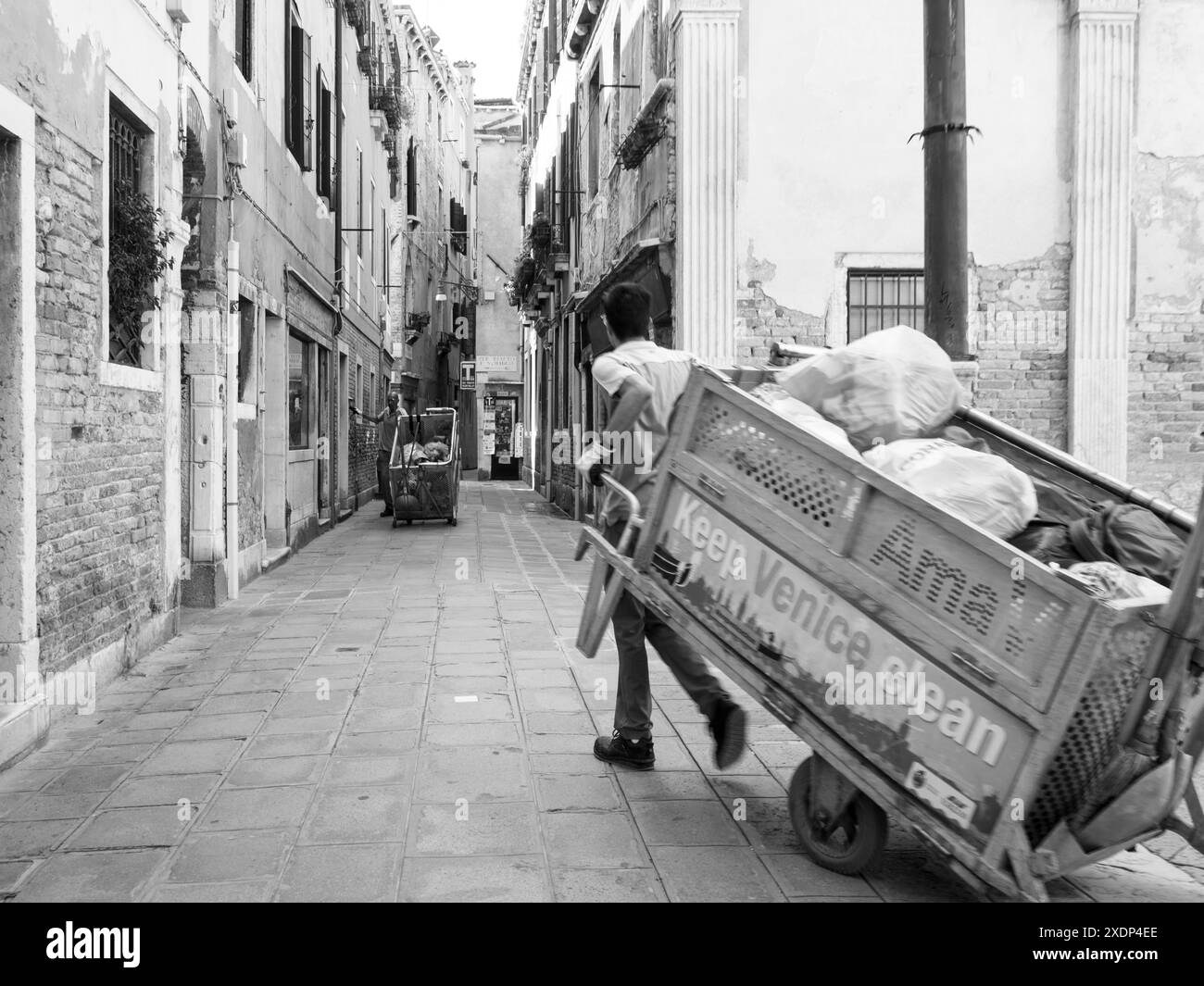 Venedig, Italien - 30. Juni 20220 Müllmann, der hart einen Wagen voller Müllsäcke in einer engen Straße von venedig schiebt Stockfoto