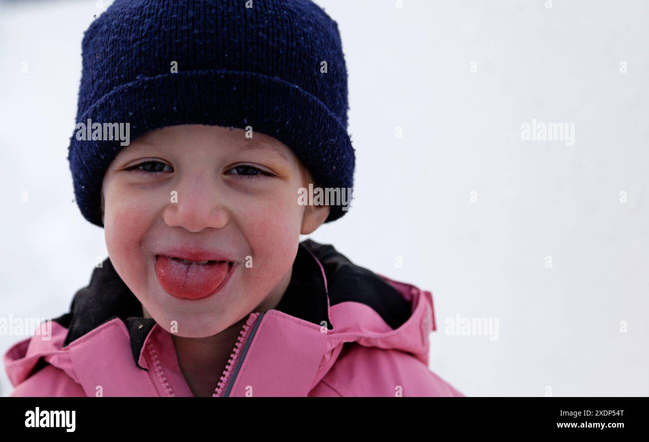 Kleines schelmiges Mädchen, vierjährige Winterzeit, die ihre Zunge neckisch ausstreckt Stockfoto
