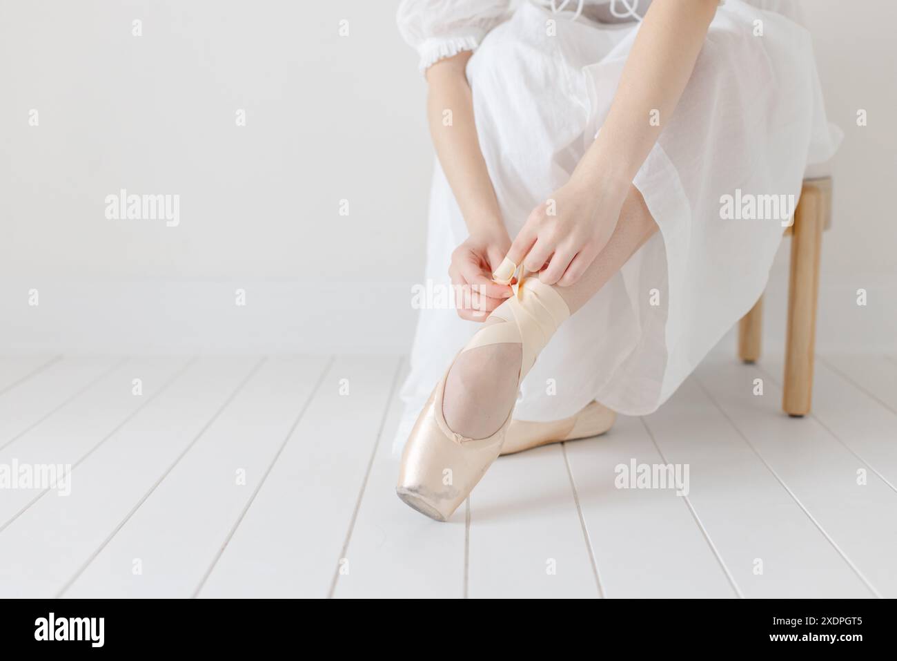 Ballerina zieht ihre spitzenschuhe im weißen Studio aus Stockfoto