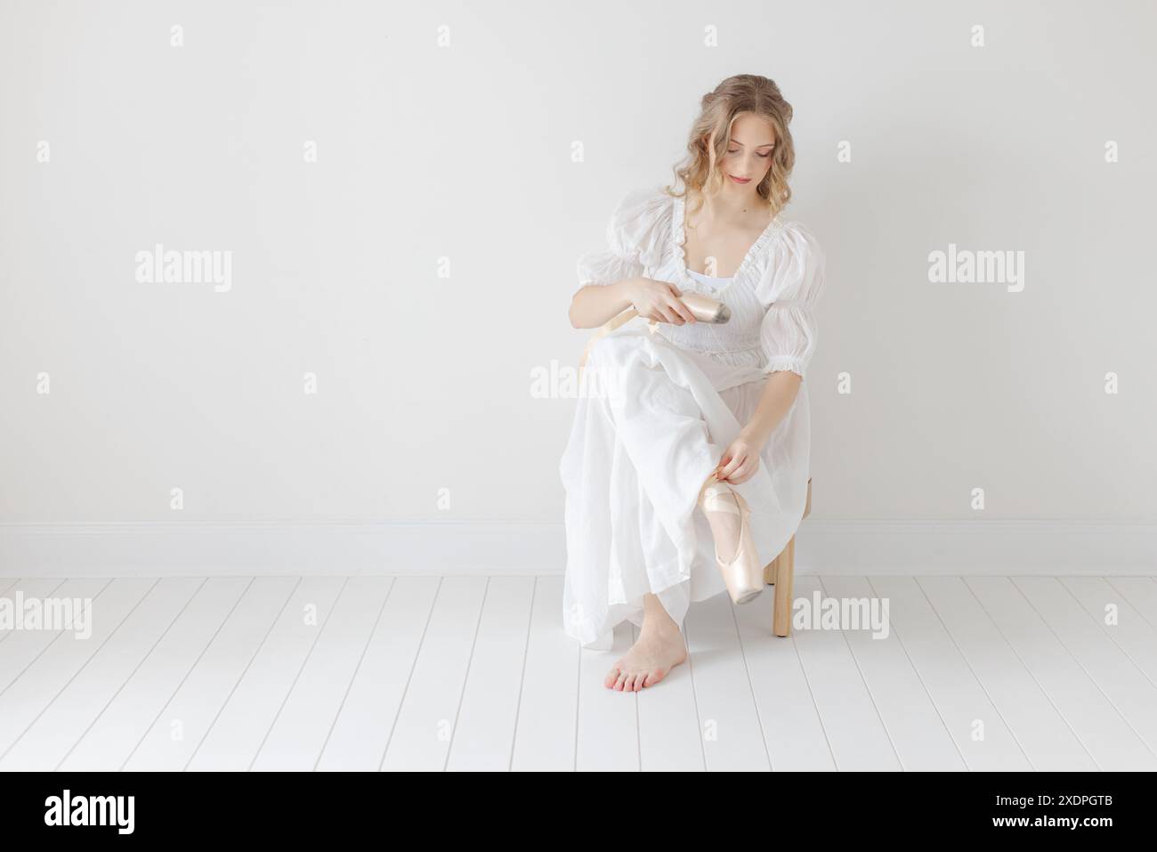 Ballerina zieht ihre spitzenschuhe im weißen Studio aus Stockfoto