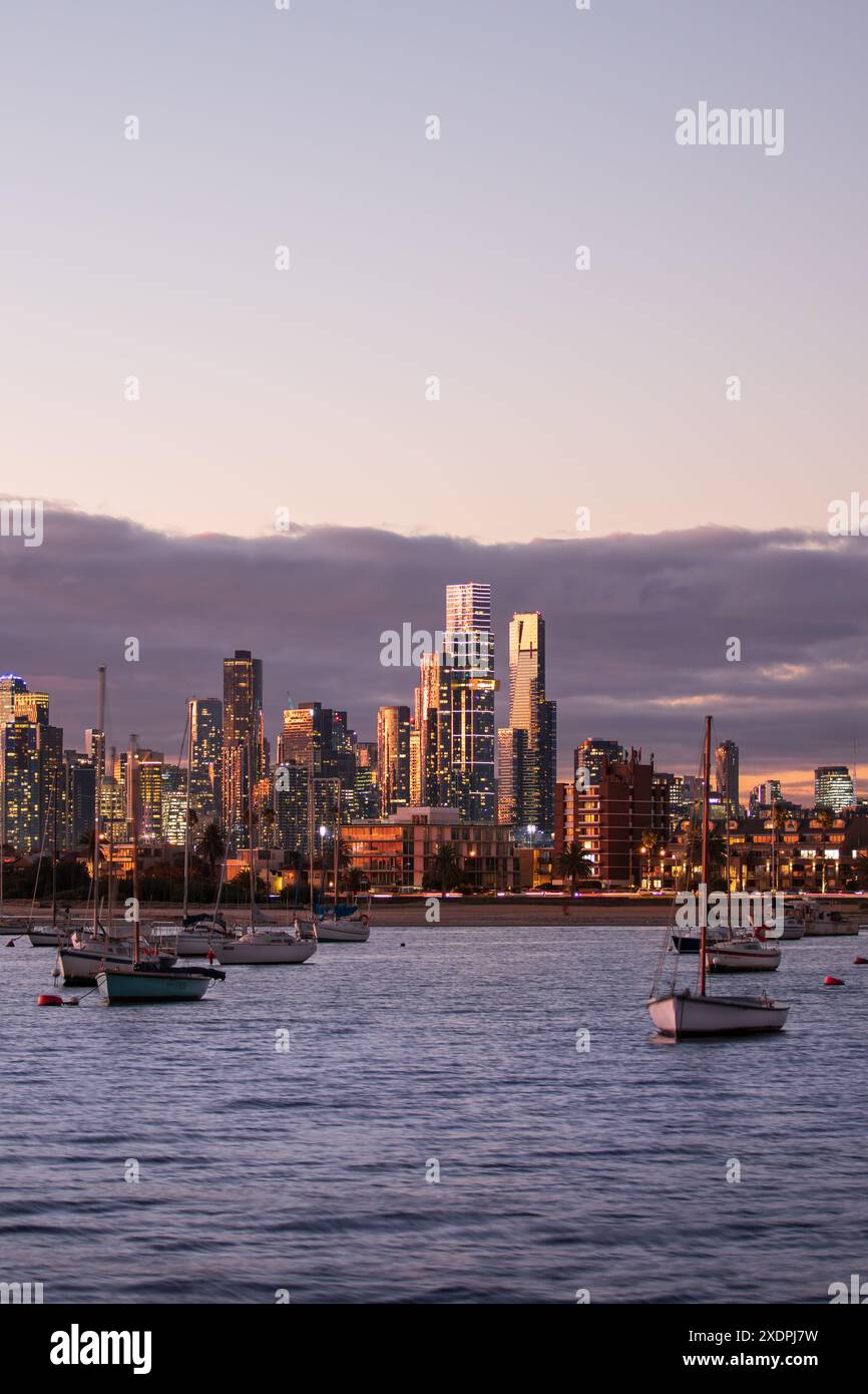 Sonnenuntergang beleuchtete Skyline von Melbourne über Port Phillip Bay mit Booten in der Abenddämmerung Stockfoto