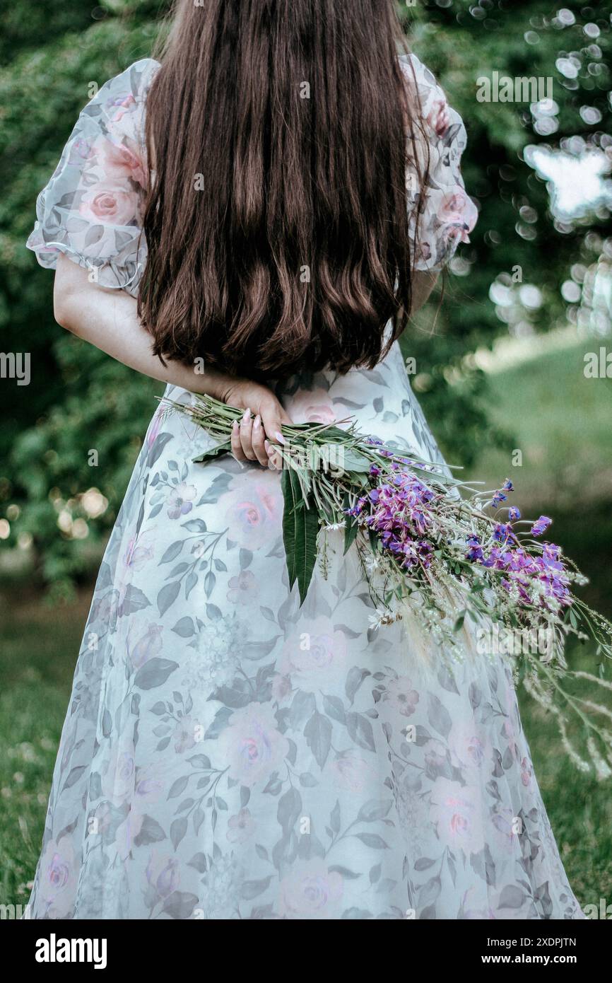 Eine junge schlanke Frau mit langen Haaren hält einen Blumenstrauß Stockfoto