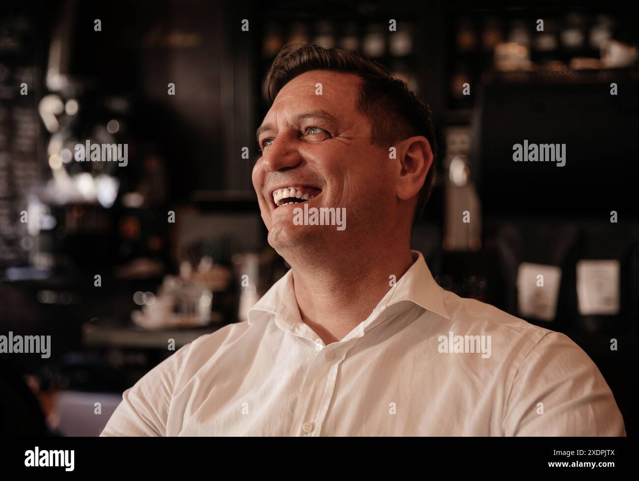 Lächelnder Mann in einem weißen Hemd, der eine Tasse Kaffee in einem trendigen Café genießt Stockfoto