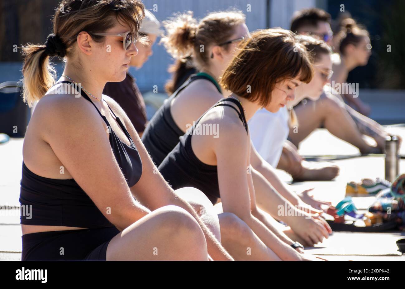 Menschen, die während des Yoga-Kurses im Freien an sonnigen Tagen in Meditation sitzen Stockfoto