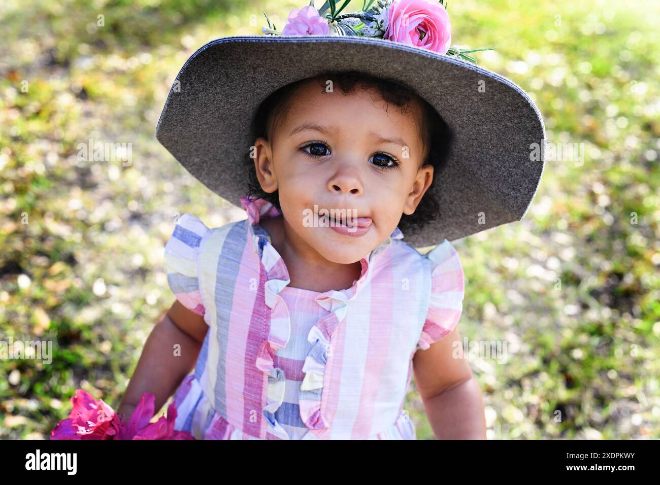 Kleinkind in einem farbenfrohen Kleid und Hut mit Blumen, die rausragen Stockfoto