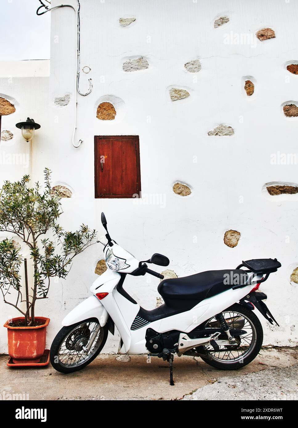 Weißes Motorrad, das vor einer weißen Steinmauer in Patmos, Griechenland, Griechenland, Europa steht Stockfoto