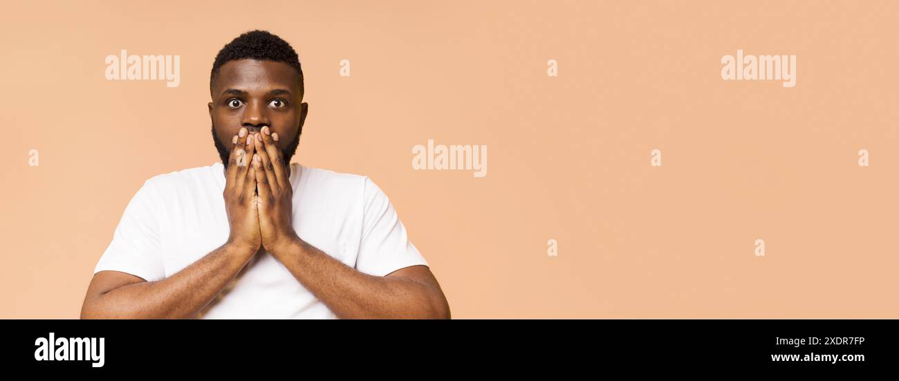 Überraschtes Black man in White T-Shirt vor Peach Studio Hintergrund Stockfoto