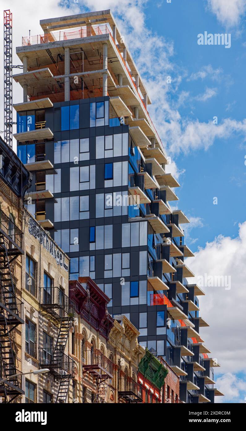 NYC Chinatown: 59 Henry Street, die sich im Bau befindet, überragt seine Nachbarn; seine Glas- und Metallpaneele treffen auf jahrhundertealte Mauerwerkstile. Stockfoto