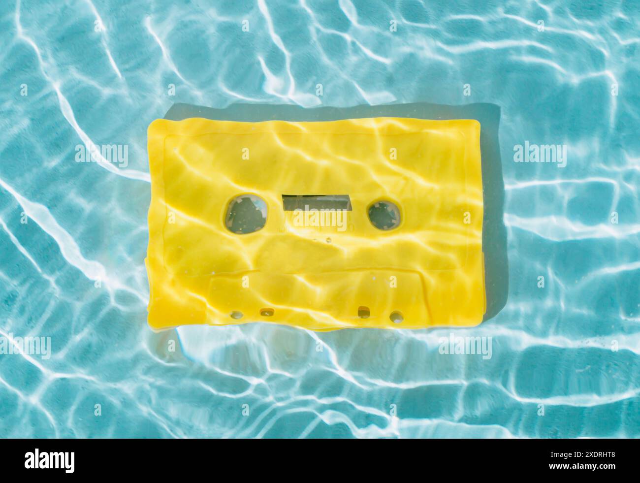 Sommerszene mit gelbem Audiokassettenband im Wasser. Sonne und Schatten. Sommer-Retro-Musikkonzept. Kreative Retro-Technologie, modischer Stil der 80er Jahre. Stockfoto