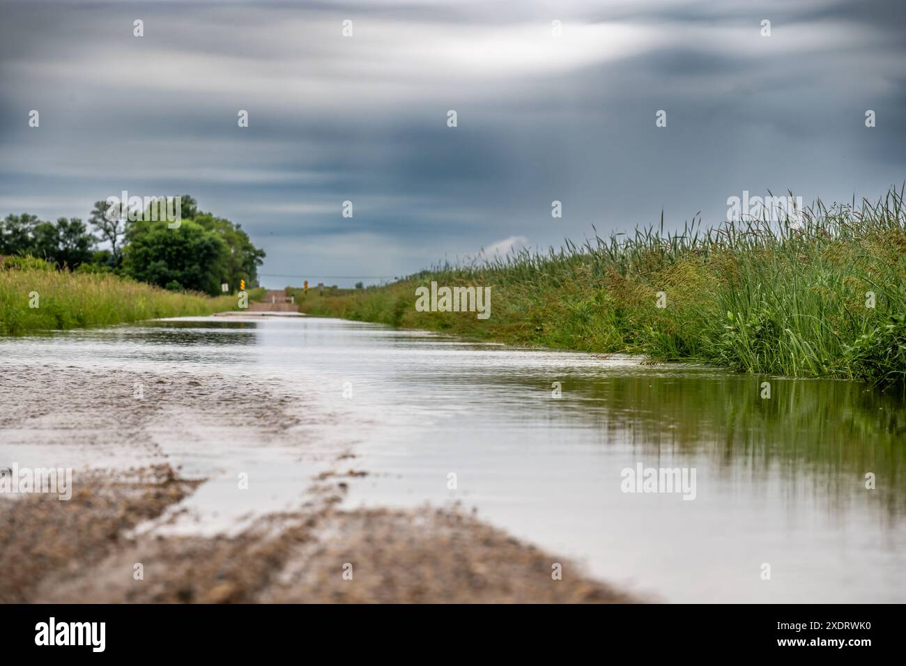 Selektiver Fokus auf den Schotter, der in Hochwasser mündet und die Straße in einem ländlichen Gebiet bedeckt Stockfoto