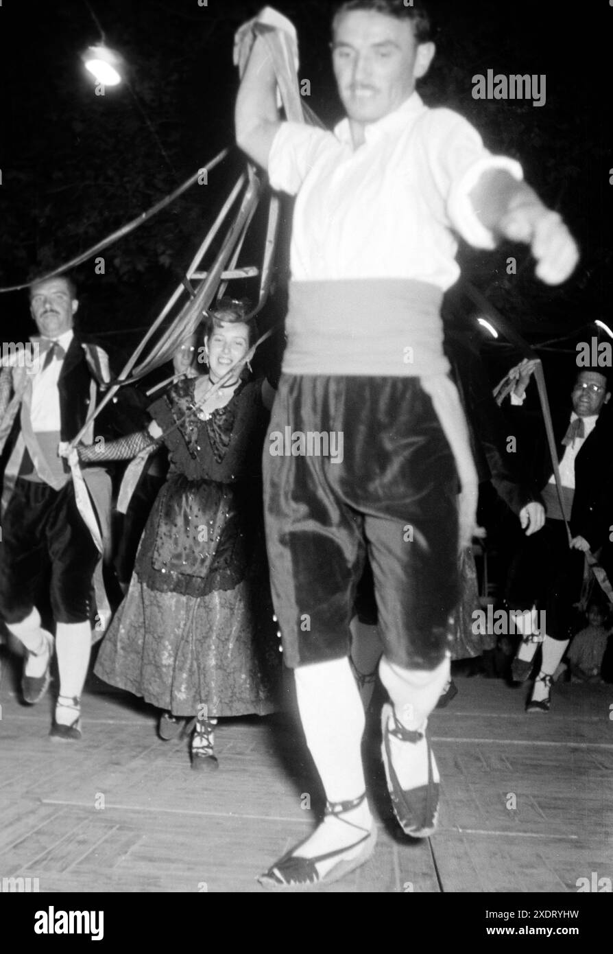 Männer und Frauen in traditioneller Kleidung führen einen Volkstanz auf der Festa Major, dem größten Volksfest in San Felíu de Guixols, auf, Katalonien 1957. Männer und Frauen in traditioneller Kleidung spielen einen Volkstanz auf der Festa Major, dem größten Volksfest in San Felíu de Guixols, Katalonien 1957. Stockfoto