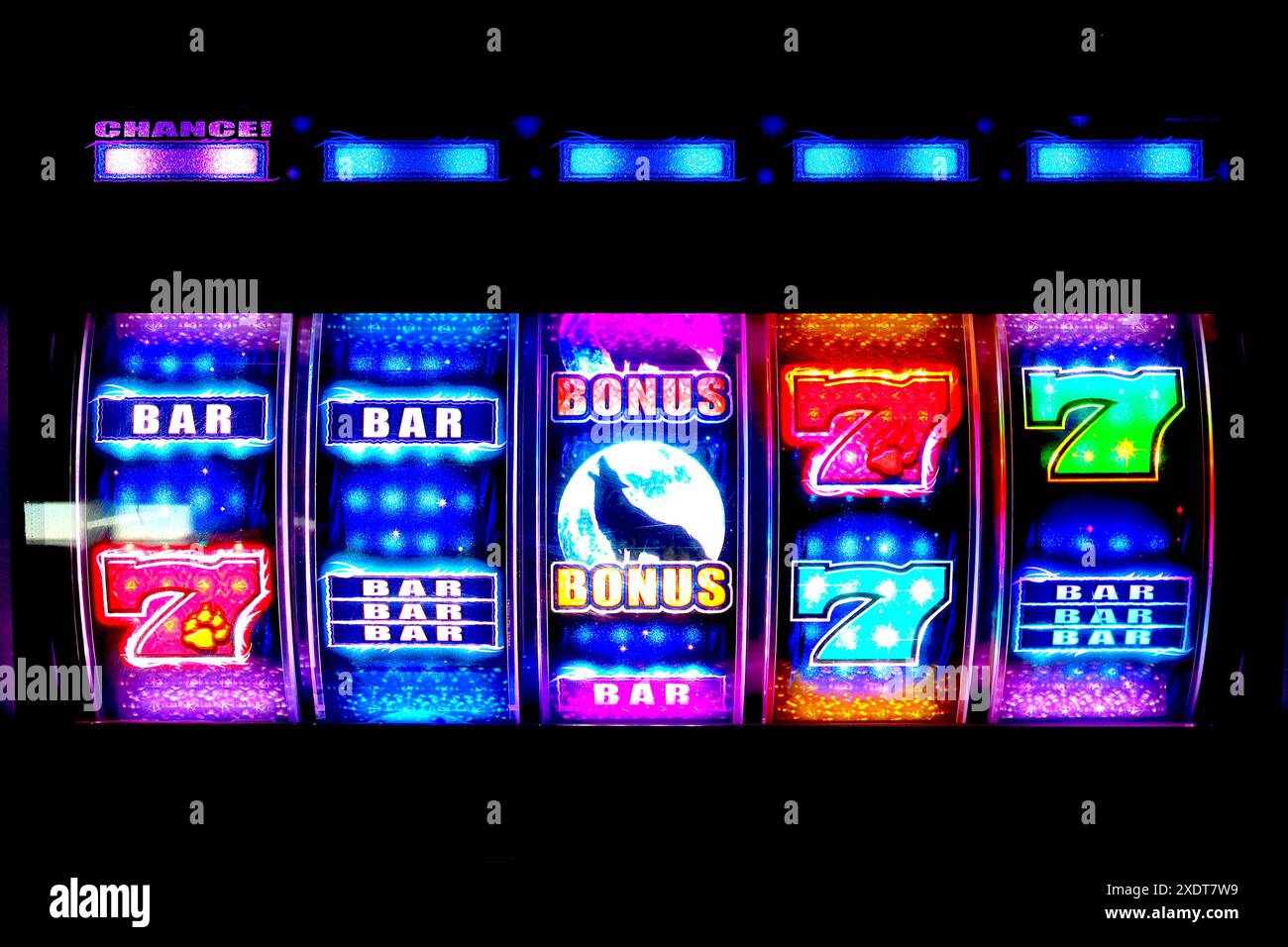 Die beleuchteten Rollen des Videospielautomaten Hewling Wolf locken Spieler mit zahlreichen blinken, farbenfrohen Grafiksequenzen in einer verdunkelten Spielhalle an. Stockfoto