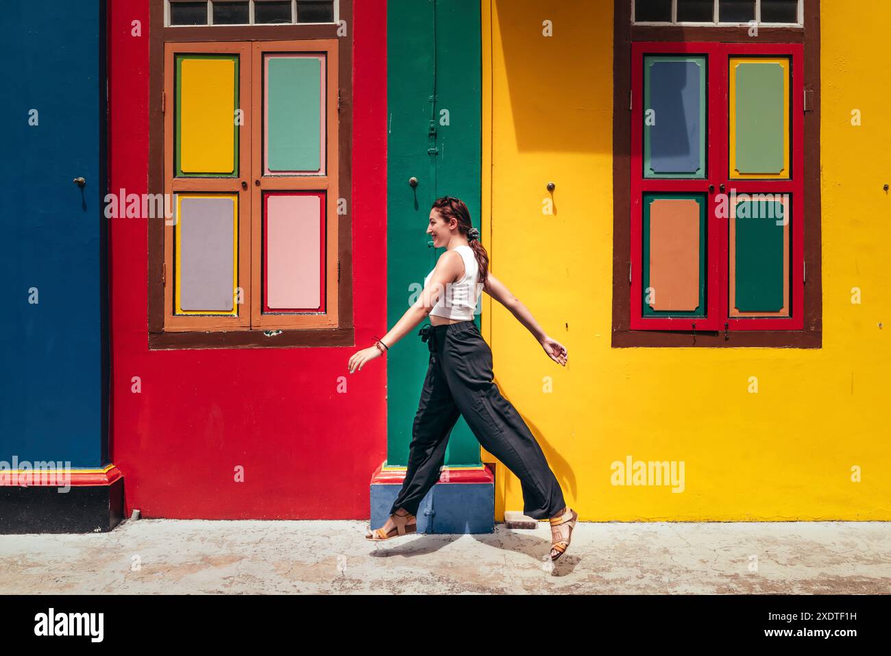 Eine Frau geht an hell bemalten Fenstern auf einer bunten Straße in Little India, Singapur, vorbei und zeigt das lebendige kulturelle Erbe der Gegend. Stockfoto
