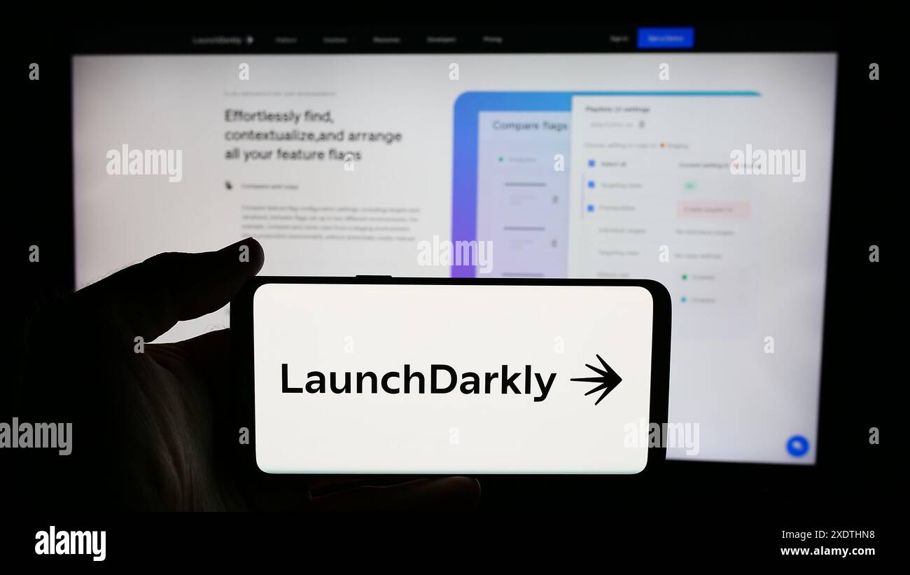 Person, die ein Mobiltelefon mit dem Logo des US-Softwareunternehmens Catamorphic Co. (LaunchDarkly) vor der Webseite des Unternehmens hält. Schwerpunkt auf dem Display des Telefons. Stockfoto