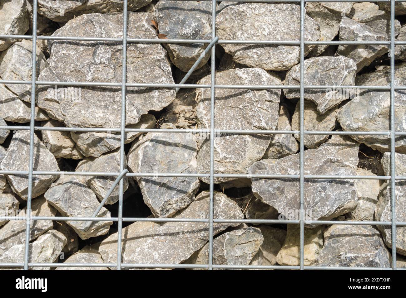 Gabion, ein Zaun aus Meeressteinen und großem blauem Glas in einer Maschenöffnung. Landschaftsgestaltung, Bauzäune, dekoratives Design für Baustellenräumung. Hohe qu Stockfoto