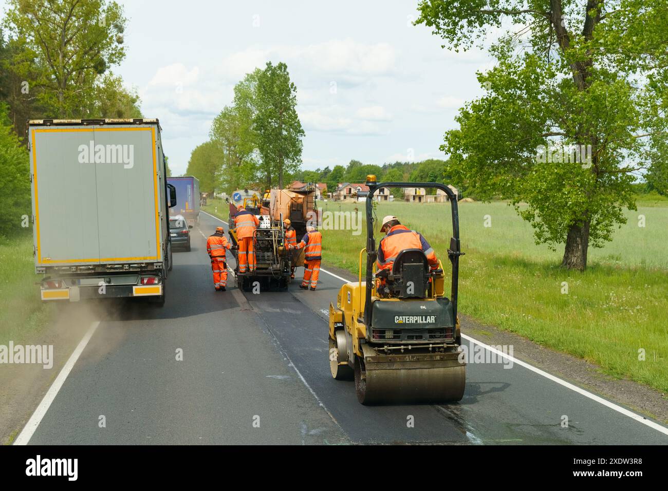 Tarnow, Polen - 19. Mai 2023: Ein Team von Arbeitern in gut sichtbarer Kleidung setzt schwere Maschinen ein, um neuen Asphalt auf einer Landstraße zu legen Stockfoto