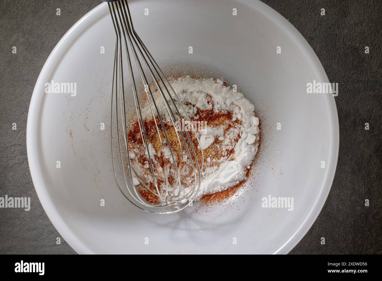 Gewürze mit Salz und Backpulver werden in einer weißen Schüssel auf dem Küchentisch, Blick von oben, gemischt. Verfahren zur Herstellung knuspriger Hühnerflügel Stockfoto