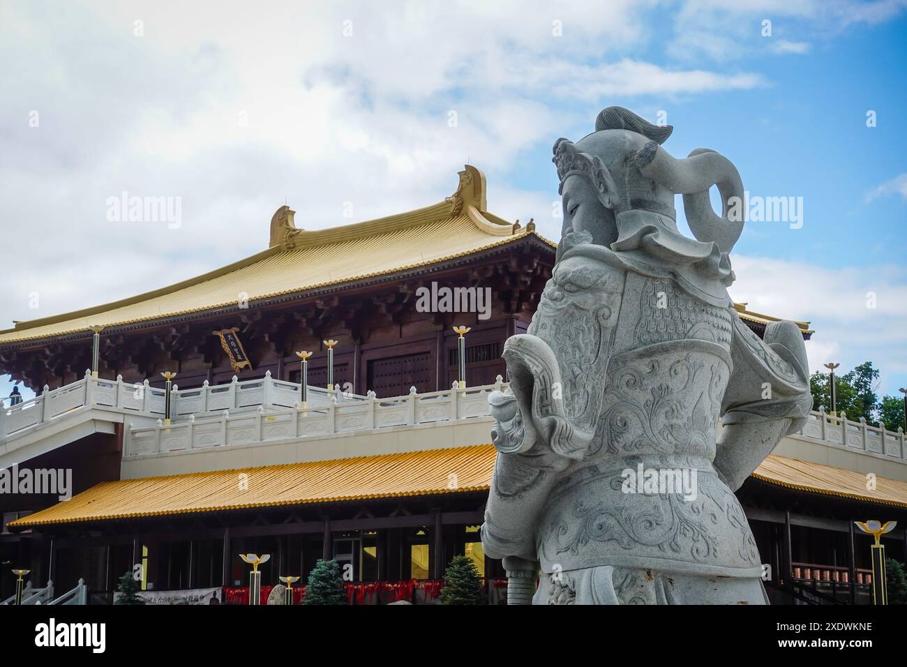 Blick auf die General Kwan Statue mit der majestätischen Haupt-Buddha-Halle im Hintergrund im Wutai Shan Buddhist Garden, Kanada. Stockfoto