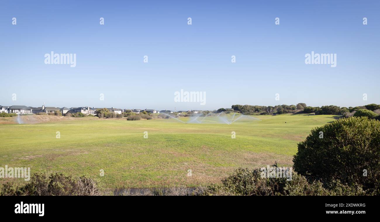 Sprinkler bewässern grünen Rasen in Vorstadtviertel an sonnigen Tagen, Kopierraum Stockfoto