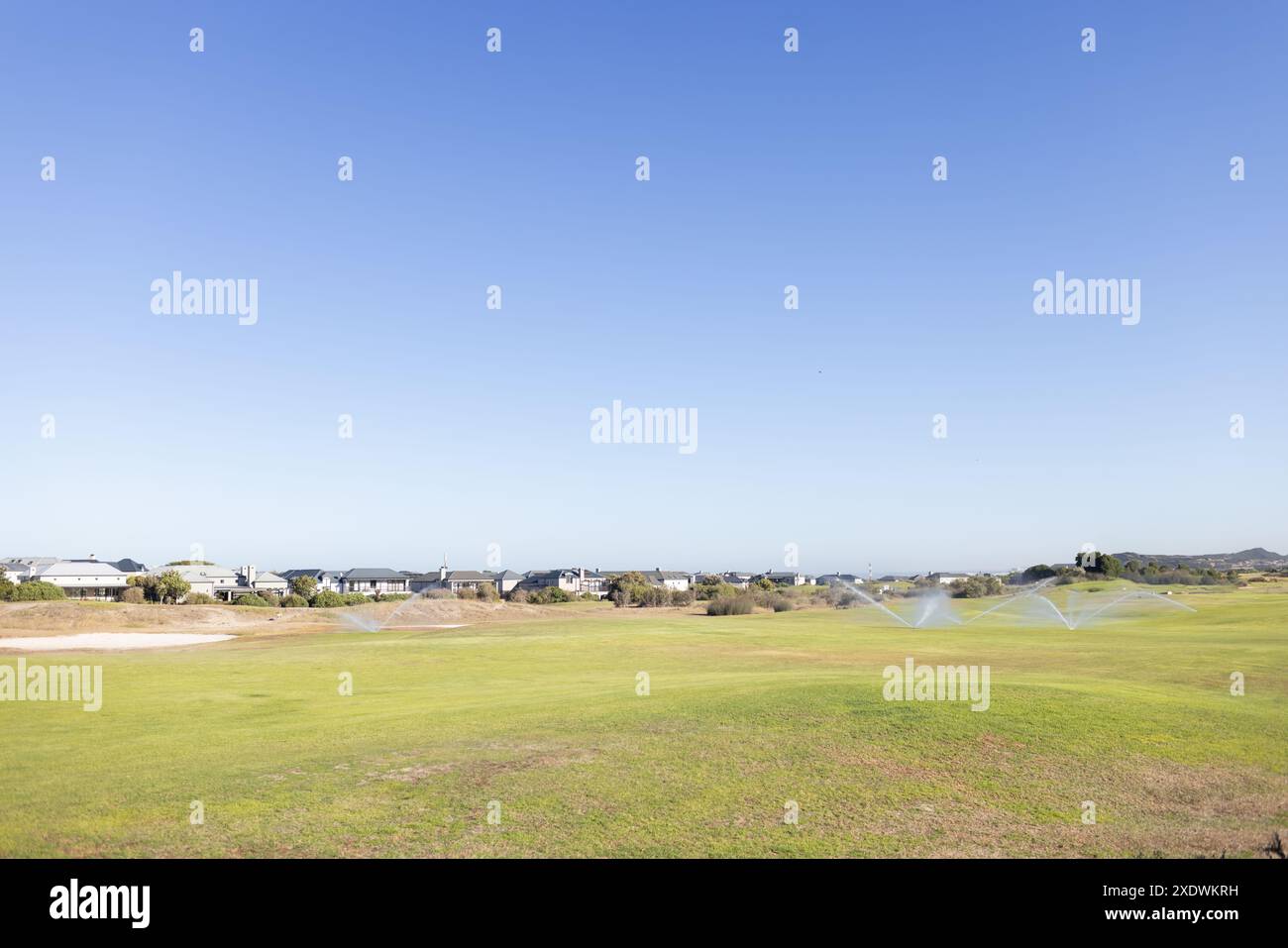 Sprinkler bewässern grünen Rasen in Wohngegend an sonnigen Tagen, Kopierraum Stockfoto