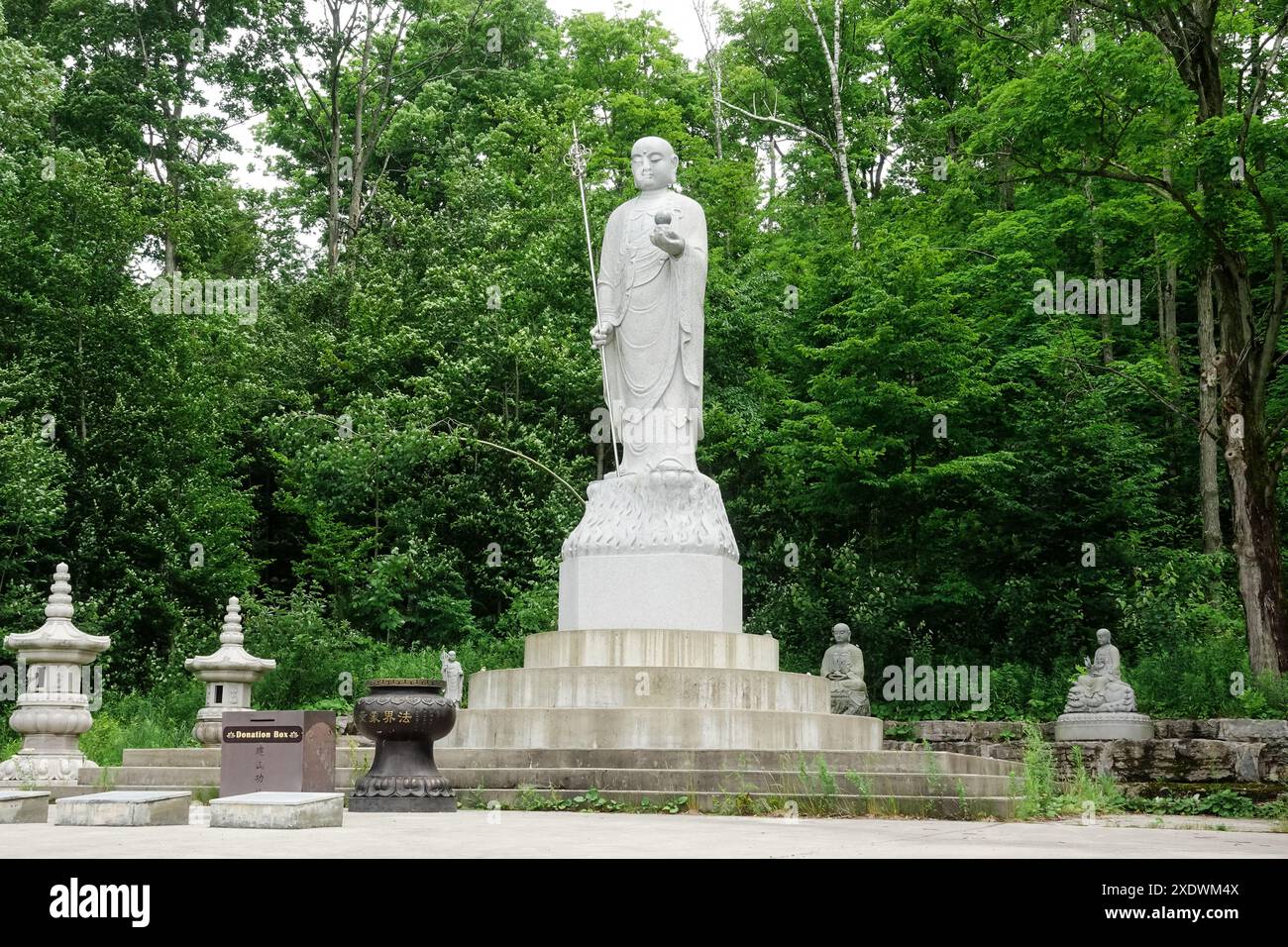 Hohe weiße Ksitigarbha Bodhisattva Statue mit Waldhintergrund im Wutai Shan Buddhist Garden, Kanada Stockfoto