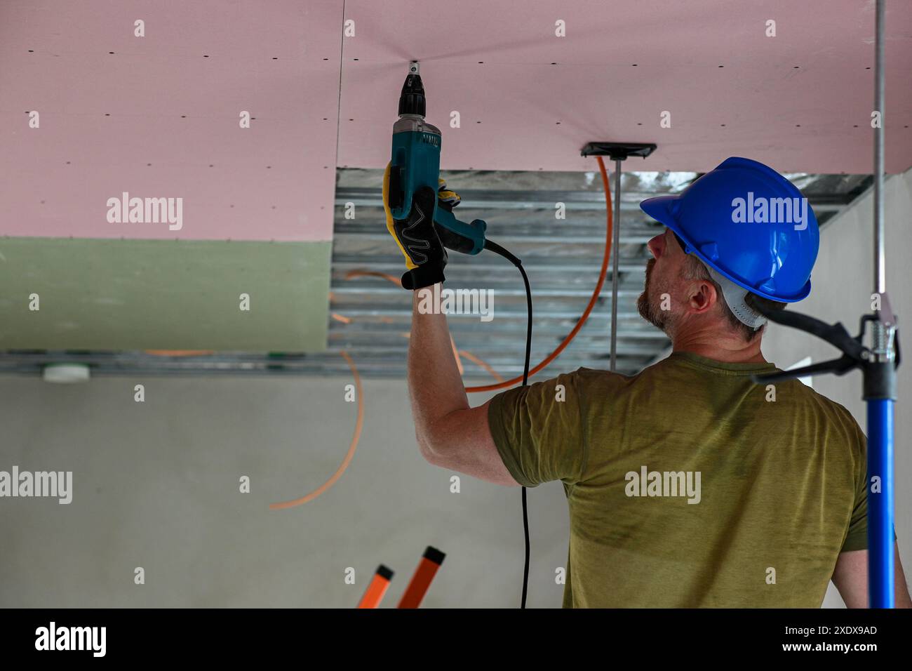 Bauarbeiter tragen Schutzausrüstung mit Bohrmaschine, um Trockenbauwände an der Decke in neuen Wohngebäuden zu installieren. Stockfoto