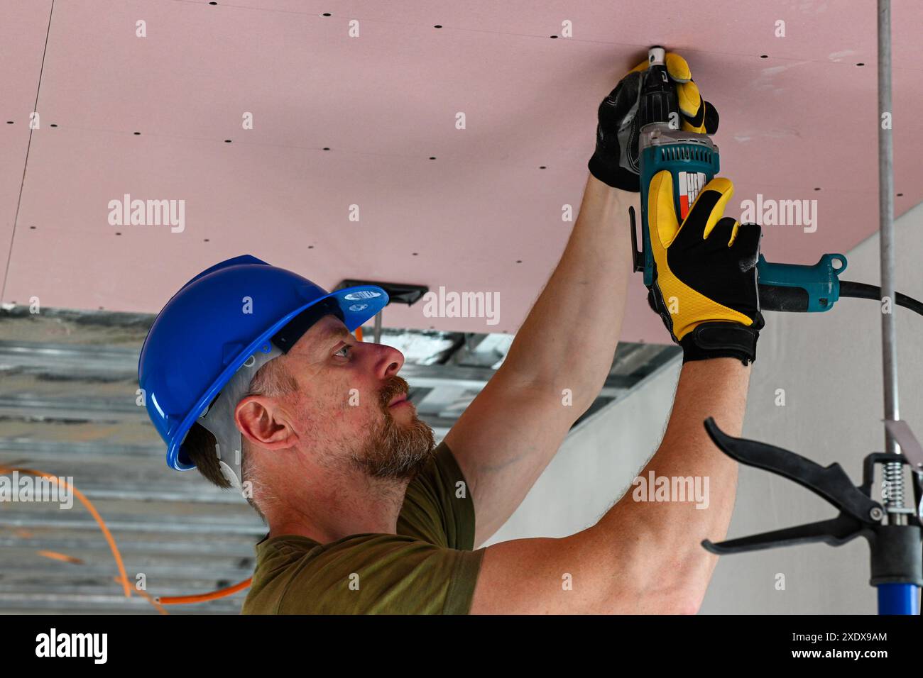 Bauarbeiter tragen Schutzausrüstung mit Bohrmaschine, um Trockenbauwände an der Decke in neuen Wohngebäuden zu installieren. Stockfoto