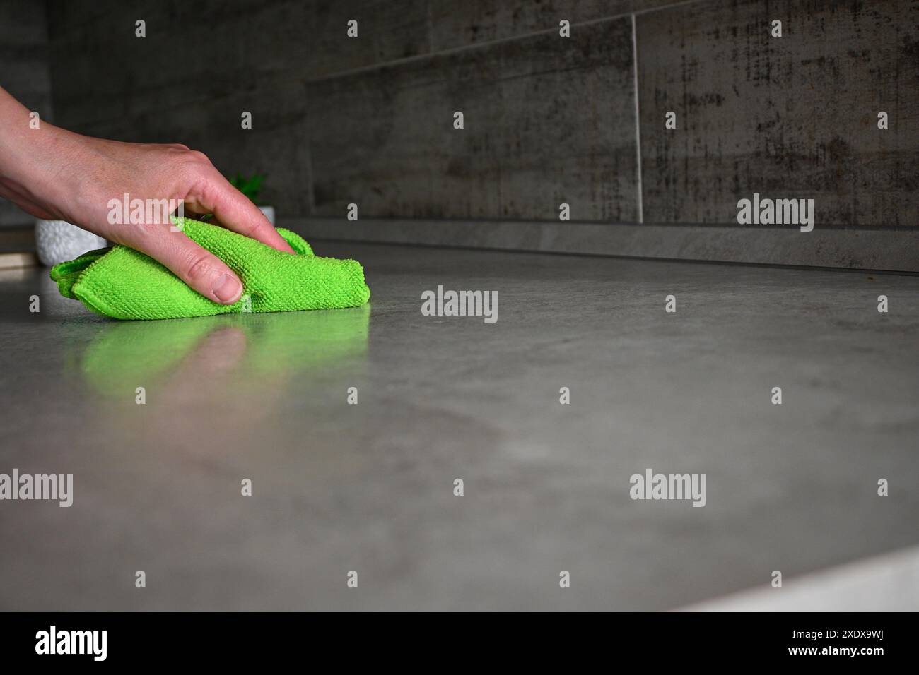 Haushälterin, die grauen Küchenarbeitsplatten mit grünem Mikrofasertuch reinigt. Stockfoto