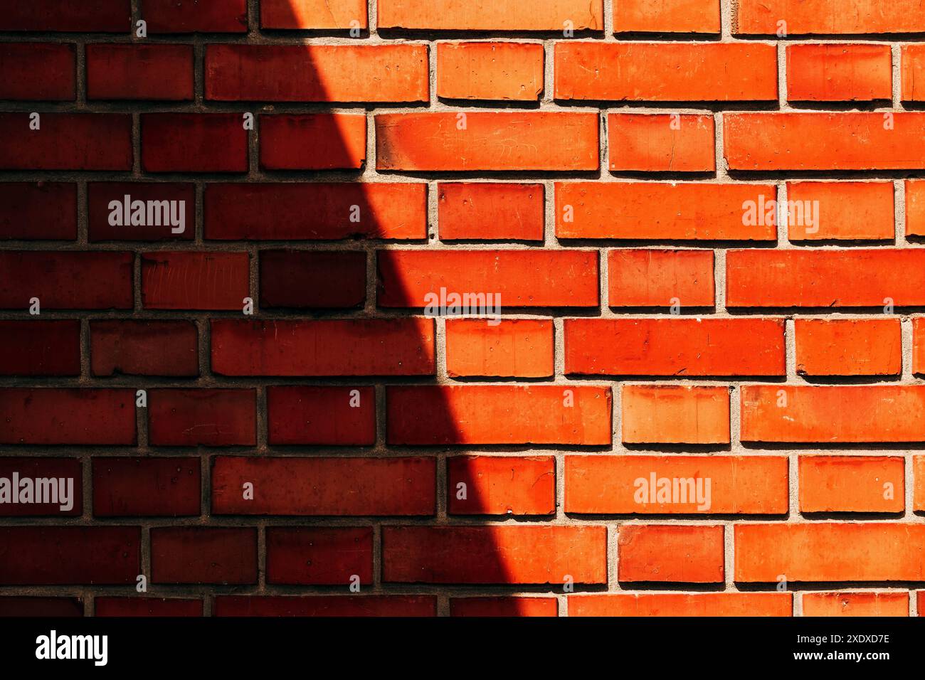 Orangefarbene Ziegelwand mit rauem Sonnenlicht und dunklem Schatten über dem Mauerwerk als Hintergrund Stockfoto