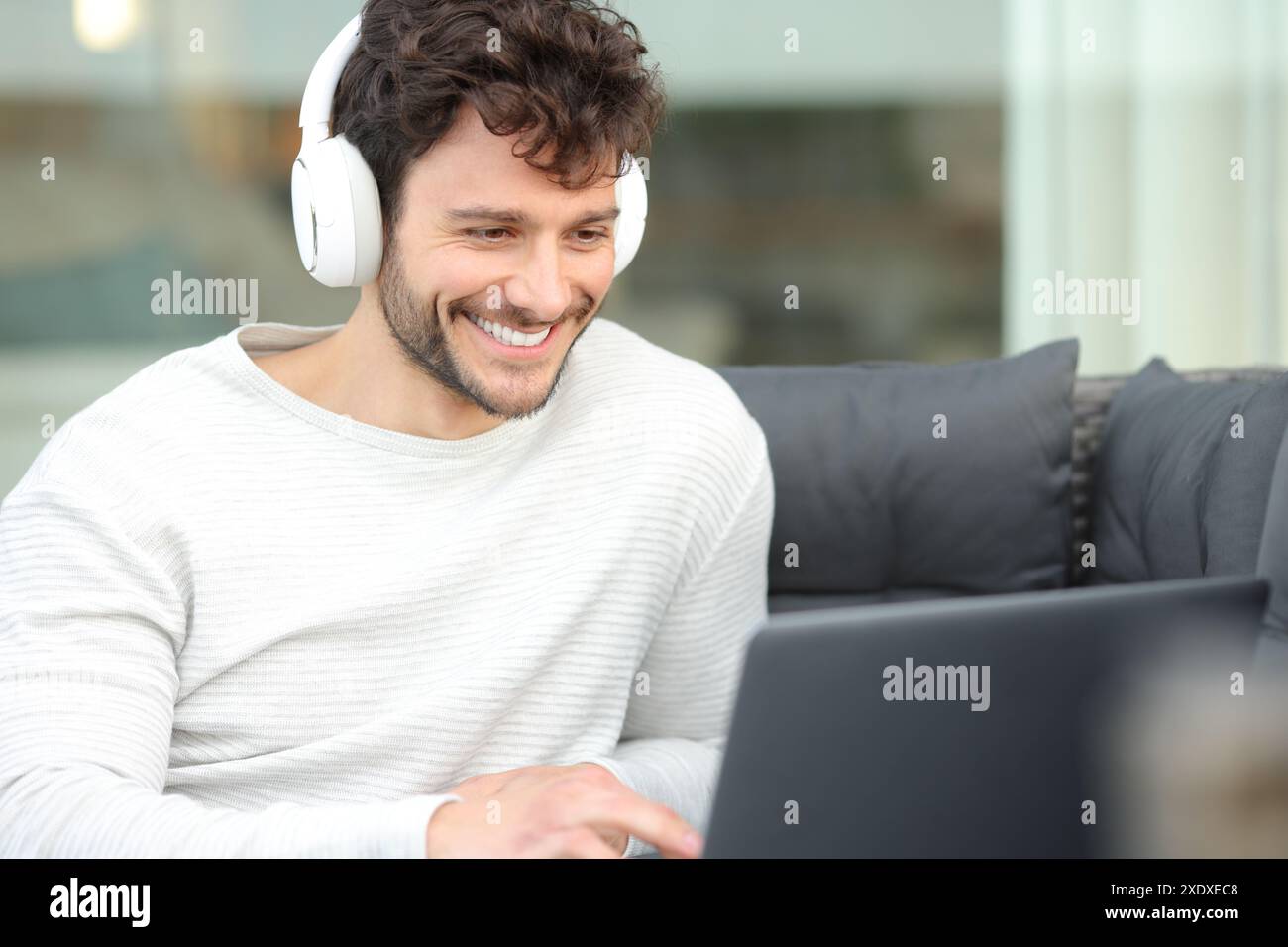 Glücklicher Mann mit Kopfhörern, der Medien auf einem Laptop auf einer Terrasse zu Hause ansieht Stockfoto