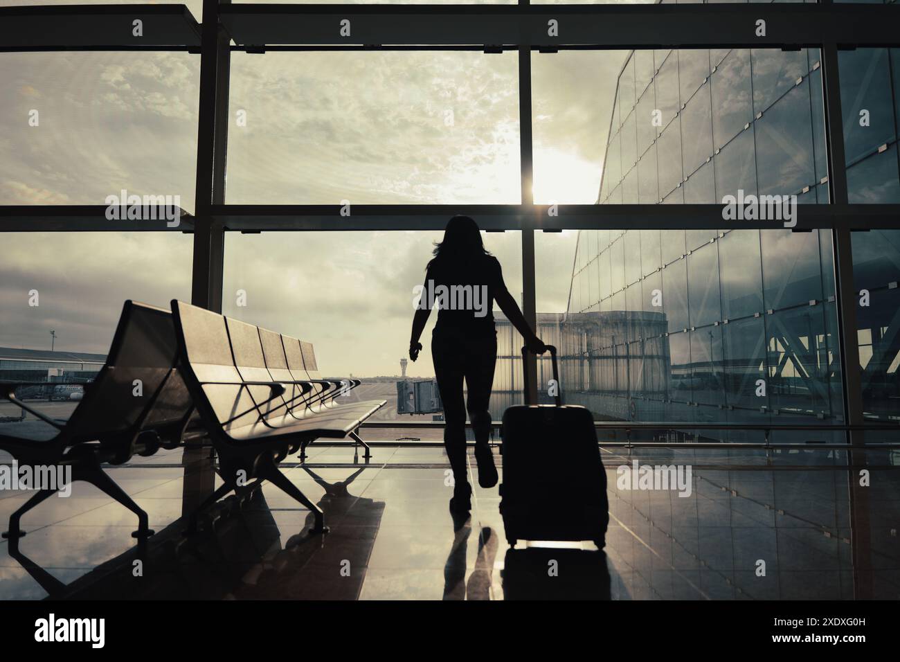 Frau mit Koffer geht durch die Abflughalle des Flughafens, während die Sonnenstrahlen durch das Fenster kommen. Stockfoto