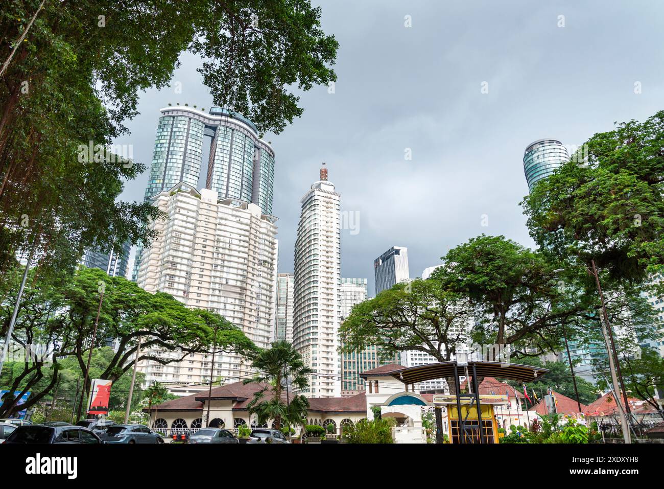 Im Stadtzentrum von KL, mit vertrauten urbanen Wahrzeichen, modernen Gebäuden im Hintergrund, umgeben von üppigen Bäumen und dunklen, regenbedrohlichen Wolken, die sich im Überfluss abzeichnen Stockfoto