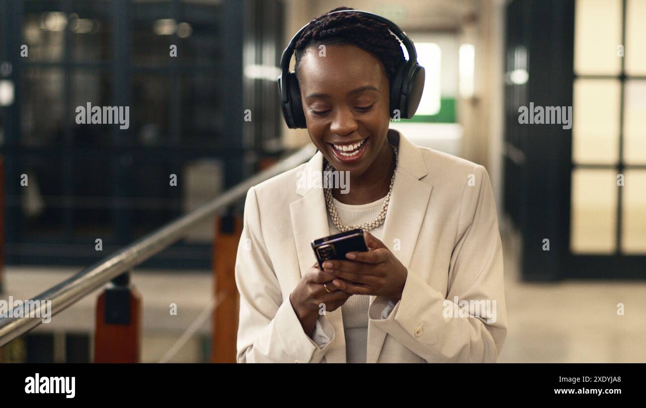 Professionelle Frau lächelt und hört Musik auf dem Smartphone in moderner Büroumgebung Stockfoto